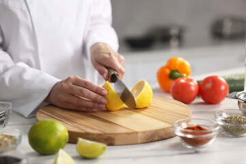 Professional chef cutting lemon at table in kitchen, closeup