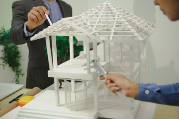 Engineers are discussing house construction plans, reviewing blueprints, assessing materials, and...