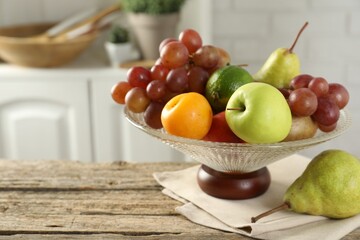 Glass vase with different fresh fruits on wooden table, closeup