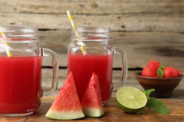 Tasty watermelon drink in mason jars and fresh fruits on wooden table, closeup