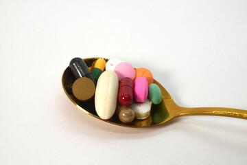 close up of colorful medicine tablets, capsules, and pills in the golden spoon on the white background isolated