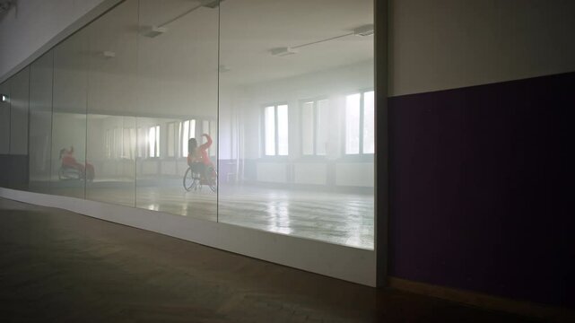 Reflection in the mirror of a woman with a disability, a para dancer practicing in a dance hall, performing a pirouette in a wheelchair, wide shot.