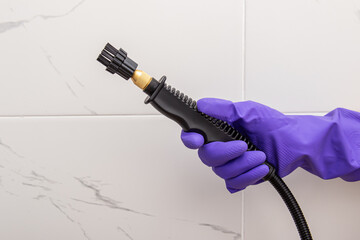 Worker in purple gloves cleans the bathroom with steam cleaner. Steam cleaner brush on tile background