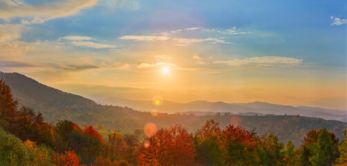 Fototapeta premium A breathtaking sunrise over a mountainous landscape. The golden light bathes the misty hills and colorful autumn trees, creating a warm, peaceful ambiance under a sky brushed with clouds