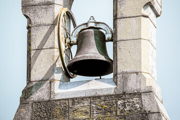 Obraz premium A large bell hangs from a stone tower. It is made of metal and has a circular frame. The tower is made of light-colored stone.