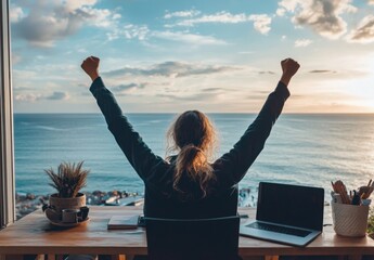 A woman sitting at her desk with arms raised in joy, celebrating success after embracing the corporate remote work lifestyle on an ocean-view balcony during sunrise.