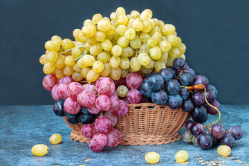 Yellow, black and red grapes in a wicker basket on a table.