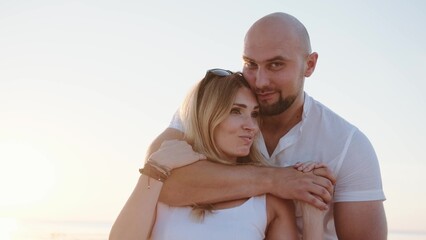 Smiling lovely couple standing on the sea coast during sunset while hugging. Romantic, relationship concept. Slow motion