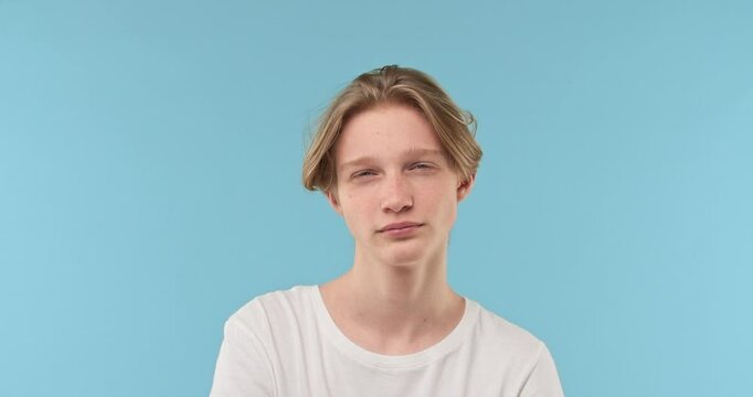 Portrait of a young guy with blond hair looking attentively at the camera on a calming blue background