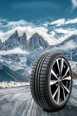 Fototapeta premium Winter tire standing on a road with snowy mountains in the background