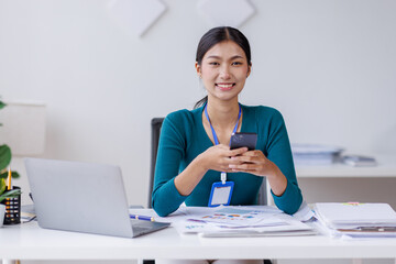 Asian woman entrepreneur busy with her work in the office. Young Asian woman work on desk laptop phone while planning sales, research or financial strategy in company
