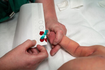 A healthcare professional carefully takes a blood sample from a babys hand, emphasizing the...