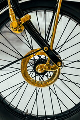 Part of the mechanism of an old wheel made of gold-colored metal against the background of black wheel spokes © annaleish