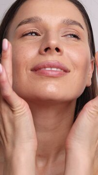 portrait of beautiful woman using bio eco cosmetic, handmade from natural ingredients.girl applying on face cheeks serum or cream, oil drops falling in palm.macro female closing eyes.studio light