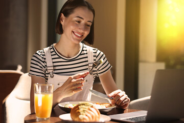 Happy woman having tasty breakfast in cafe on sunny morning