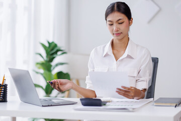 Asian Business woman using calculator and laptop for doing math finance on an office desk, tax, report, accounting, statistics, and analytical research concept
