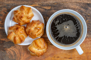 Profiteroles and cup of coffee for tasty snack over wooden background.