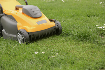 Yellow lawn mower on the spring green grass in the yard