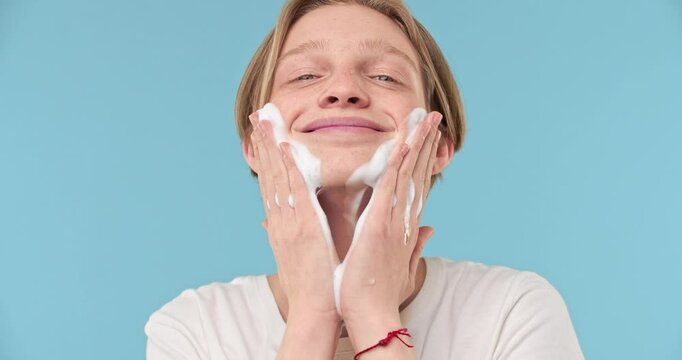 Happy young man really enjoys using gentle cleansing foam on his clean face