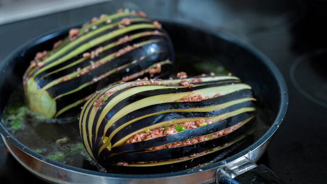 Anbraten / Schmoren von gef&auml;cherten Auberginen gef&uuml;llt mit Hackfleisch in einer Bratpfanne.