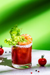 Bloody Mary cocktail variation with tomato juice, vodka, clam broth, celery, hot sauce and ice. Green background, hard light