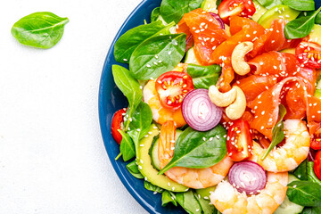 Seafood salad with shrimp, salmon, avocado, spinach, cucumber, tomato, cashew and sesame seeds.. White background, top view