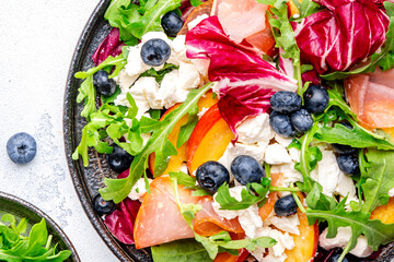 Fresh salad with arugula, radiccio, peaches, smoked ham, ricotta cheese and blueberries. White background, top view
