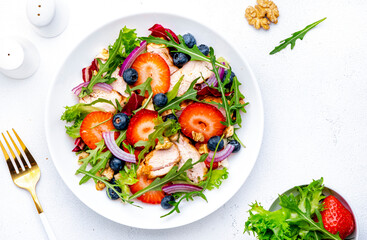 Strawberry and chicken fresh salad with arugula, blueberries, onion and walnuts, white background, top view