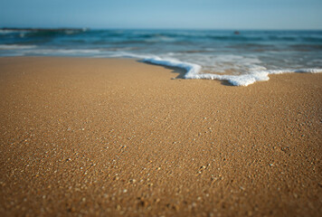 Closeup of flat smooth sand with waves and white foam diffused in the background  on a sunny day