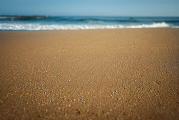 Closeup of flat smooth sand with waves diffused in the background  on a sunny day