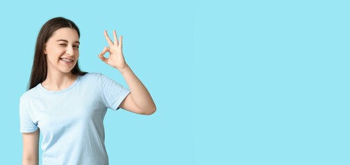 Young woman with dental braces showing OK on blue background with space for text