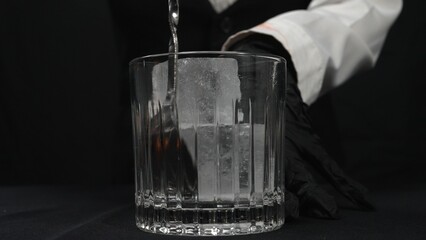 Macrography, observe the skilled hands of a female bartender expertly stirring ice in glass with ice at black background. Each close-up shot of woman prepare for making cocktail in glass. Comestible.