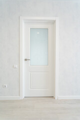 In an empty room, there stands a white door that features a glass window, adding a bit of natural light to the otherwise vacant space, enhancing the overall aesthetic of the area