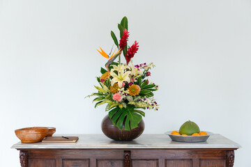 Various tropical flowers and lush green leaves in a brown vase.