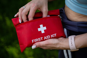 A woman is firmly holding a bright red first aid kit in her hand, prepared for any emergency...