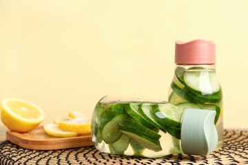 Sports bottles of infused water with cucumber slices on beige background