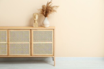 Wooden chest of drawers with pampas grass and decor near beige wall in room