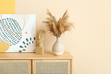 Wooden chest of drawers with pampas grass and painting near beige wall in room, closeup