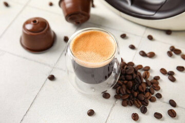 Glass of delicious espresso, pods and beans on white tiled table