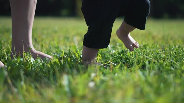 Mother guides toddler first steps grass. Toddler learns to walk outdoors. moment as toddler takes first steps with mother support. Concept toddler mother first steps. Baby milestone moment with mother