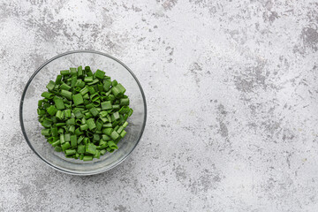 Glass bowl with slices of fresh green onion on grey background