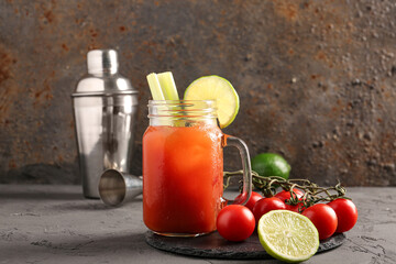 Mason jar of bloody mary with celery and shaker on grey table