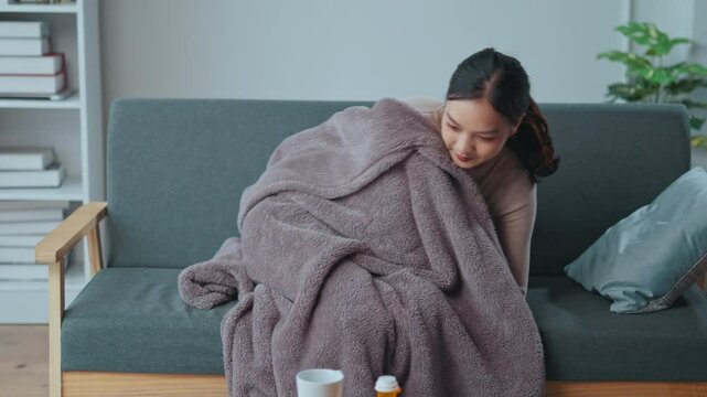 Young woman is experiencing the symptoms of a cold or flu. She takes medicine and drinks a hot beverage in hopes of feeling better