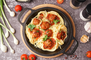 Frying pan of boiled pasta with tomato sauce and meat balls on grey table