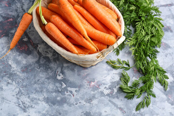 Wicker basket with fresh carrots on blue background