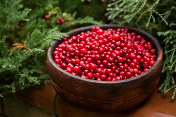 Wooden bowl of ripe juicy lingonberries on a wooden background
