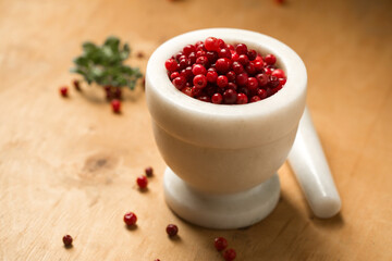 A white mortar full of ripe wild lingonberries, on a wooden background