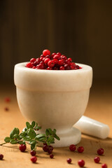 A white stone mortar full of wild lingonberries, on a wooden background, low angle