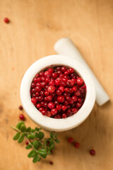 A white stone mortar full of ripe lingonberries, on a wooden background