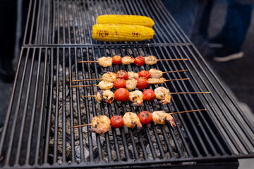 There is a grill that features an enticing combination of shrimp, ripe tomatoes, and fresh corn on the cob placed onto it, creating a delightful outdoor cooking experience